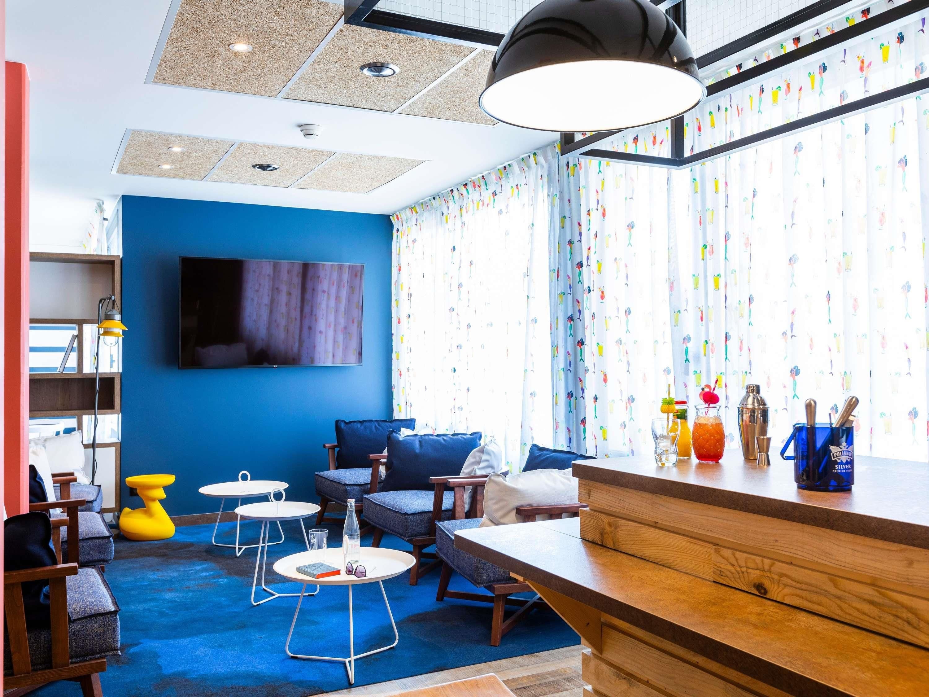 Et moderne værelse med blå væg, et fladskærms-TV, et træskrivebord og en bar med cocktailglas og en flaske.