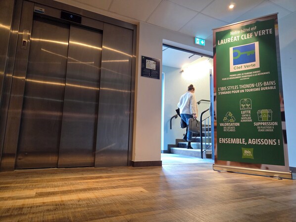 An elevator, a staircase, and a green sign with text about sustainable tourism. - ibis Styles Thonon Les Bains Hotel (Thonon-les-Bains)