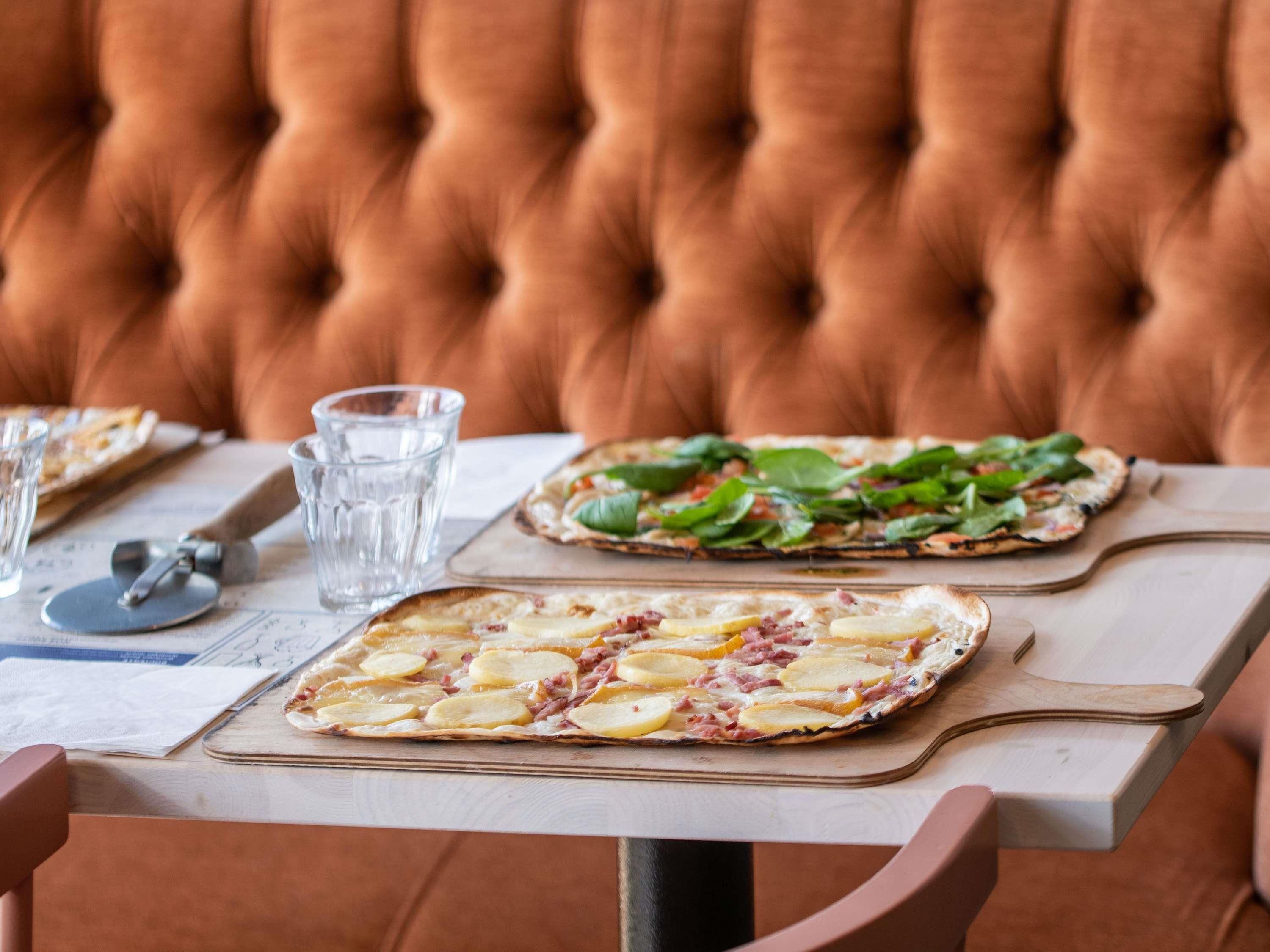 A dining table with two pizzas, a pizza cutter, and a glass of water.