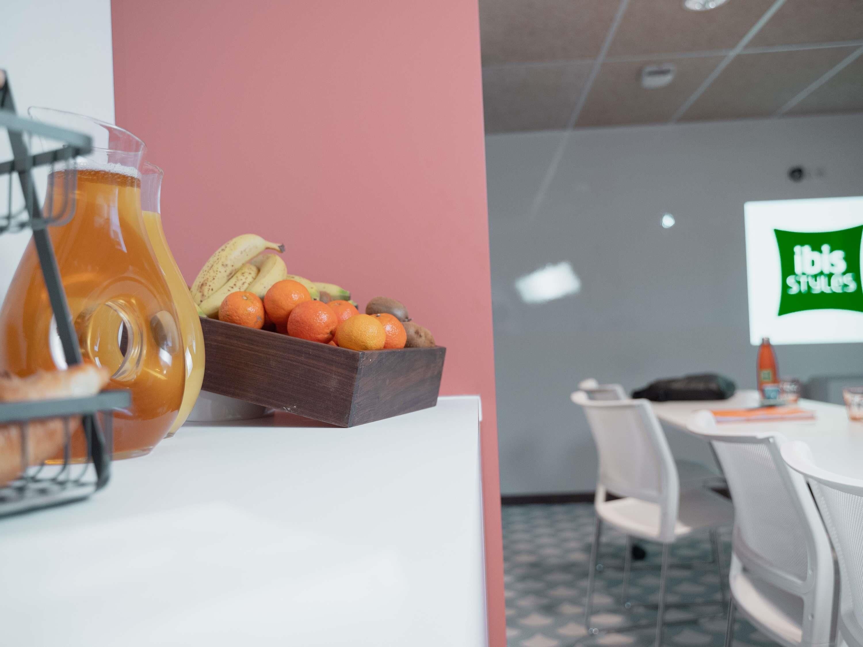 A breakfast setup with a fruit bowl and a pitcher of orange juice on a white table.