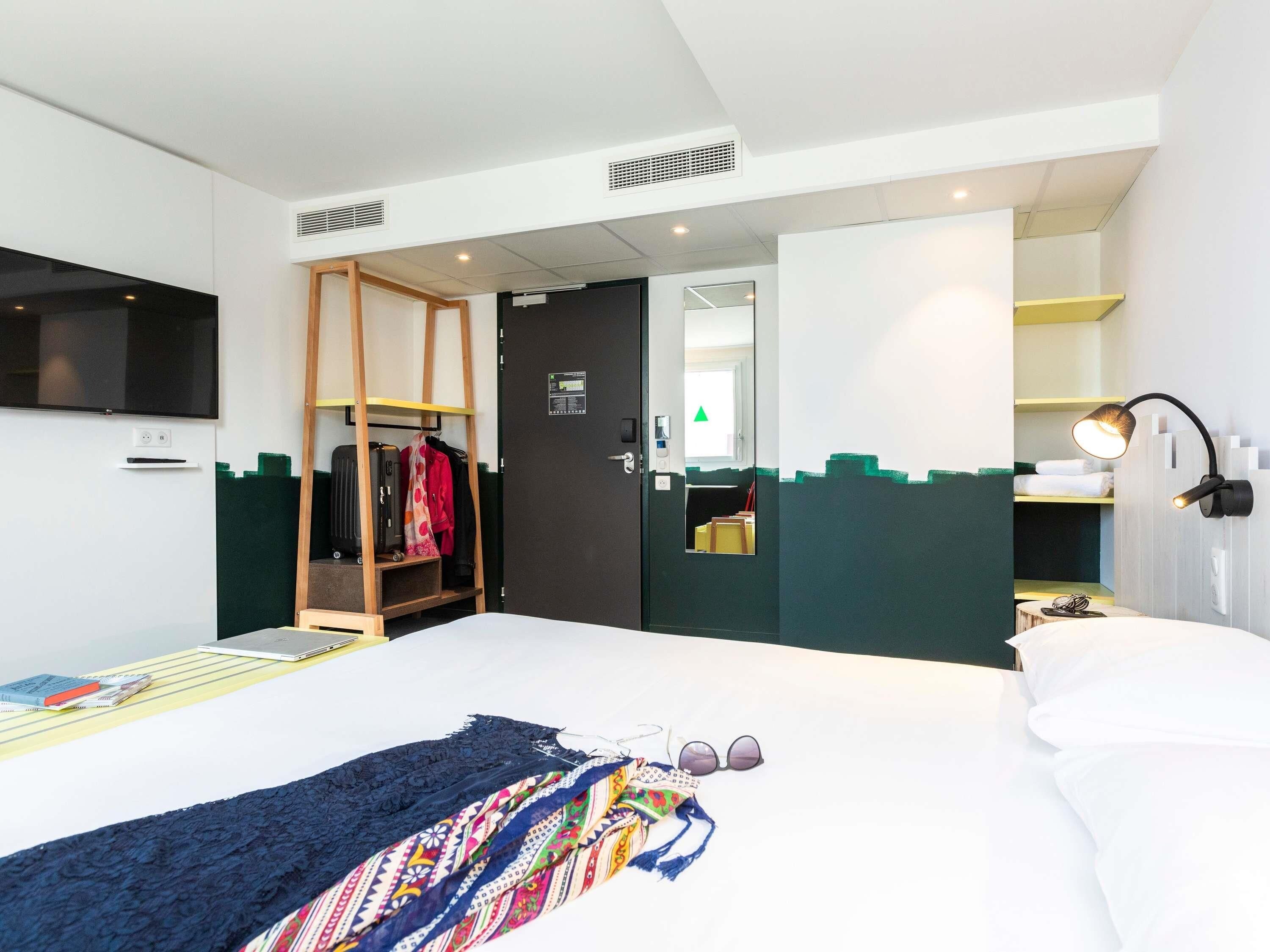 A modern hotel room with a bed, a wardrobe, a mirror, a desk, and a TV.