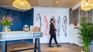 A modern interior with a wooden floor, a blue accent wall, a table with a vase of flowers, a laptop, and a wall with fish illustrations. - ibis Styles Thonon Les Bains Hotel (Thonon-les-Bains)