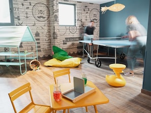 A room with a wooden wall, a table with a laptop, chairs, and a ping pong table. - ibis Styles Thonon Les Bains Hotel (Thonon-les-Bains)