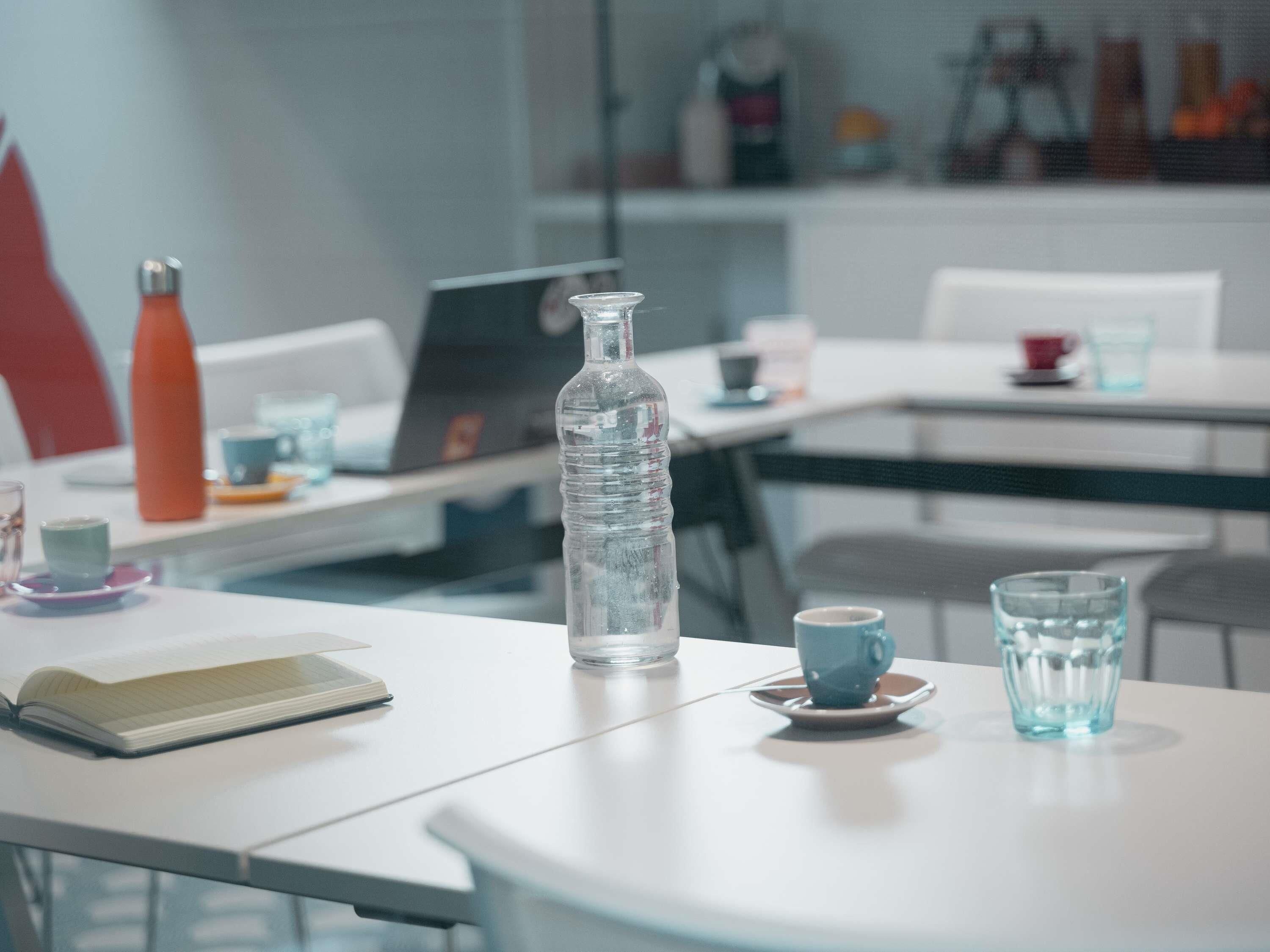 A modern office space with a white table, a laptop, a water bottle, a notebook, and a cup.