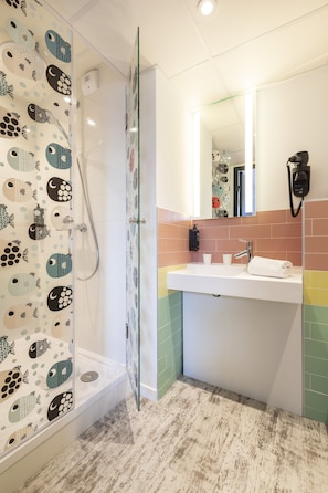 A bathroom with a glass-enclosed shower, a white sink with a mirror, and a towel on the counter. - ibis Styles Thonon Les Bains Hotel (Thonon-les-Bains)