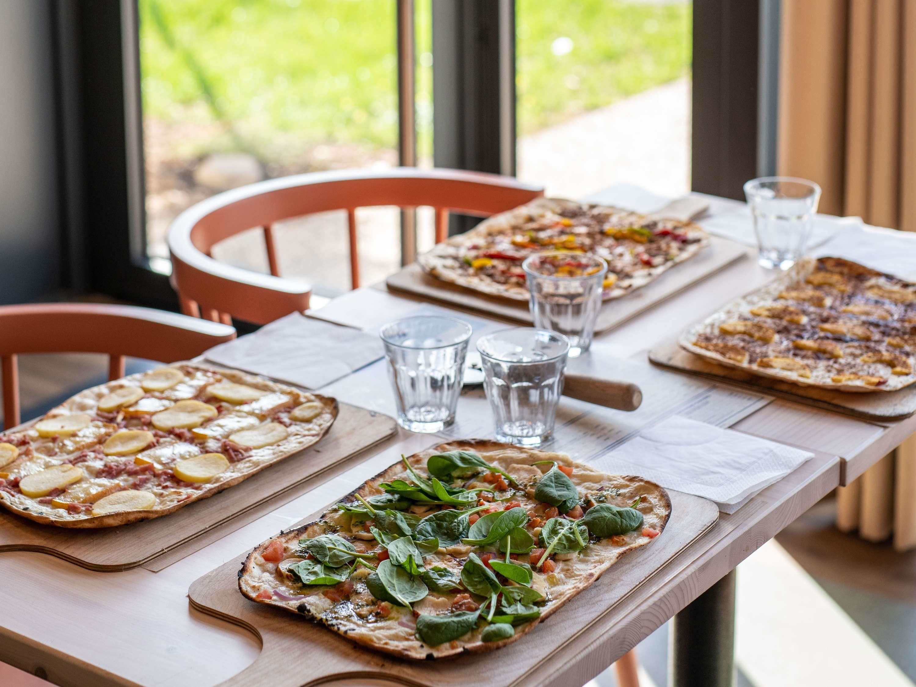 Una mesa de comedor con tres pizzas, vasos de agua y una silla de madera.