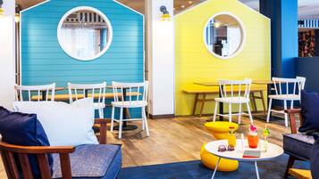 A children's play area with two house-shaped play structures, wooden tables, and white chairs.