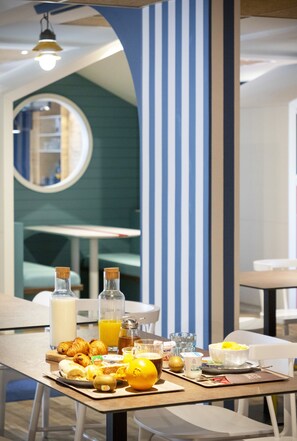 A breakfast table with croissants, orange juice, and a bowl of fruit. - ibis Styles Thonon Les Bains Hotel (Thonon-les-Bains)