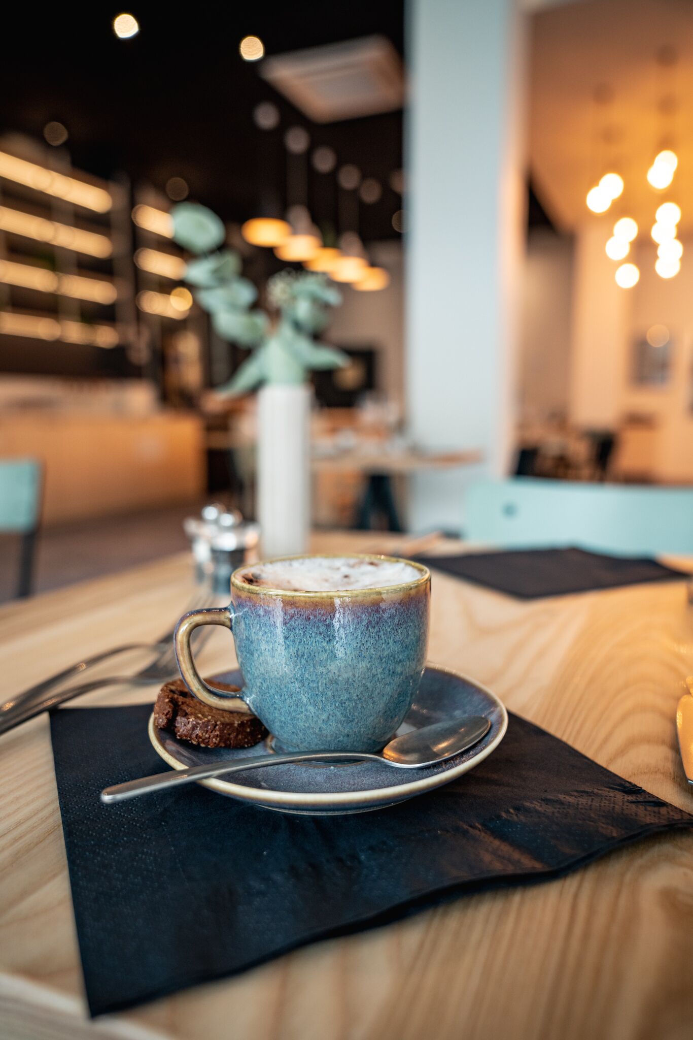A cup of coffee on a saucer with a spoon, placed on a napkin on a wooden table.