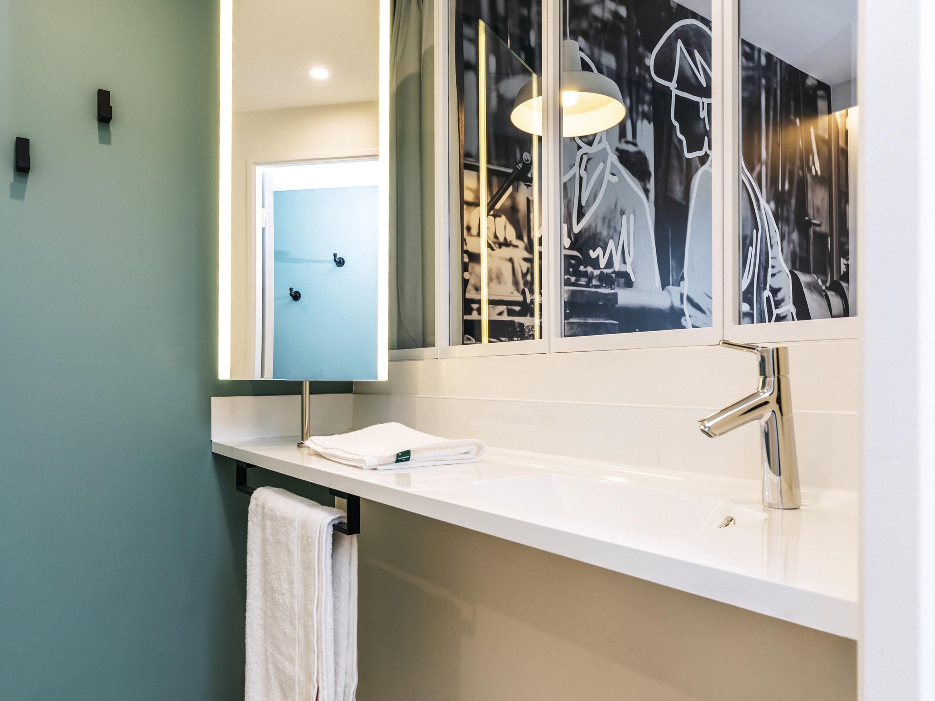 A modern bathroom with a white sink, a large mirror, and a towel rack.