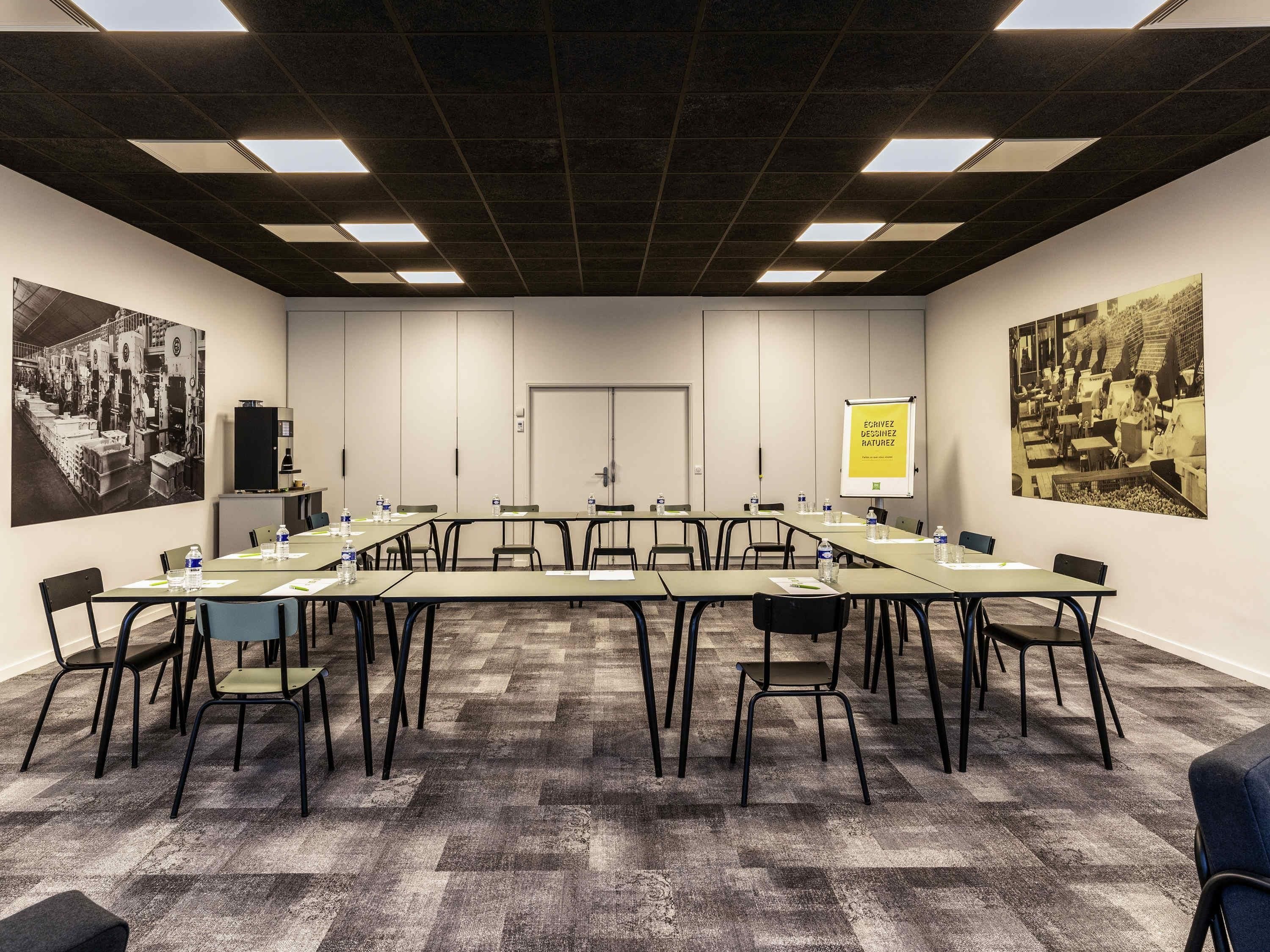 Un salón de conferencias con una larga mesa, sillas, una pizarra y dos fotografías grandes en blanco y negro en las paredes.