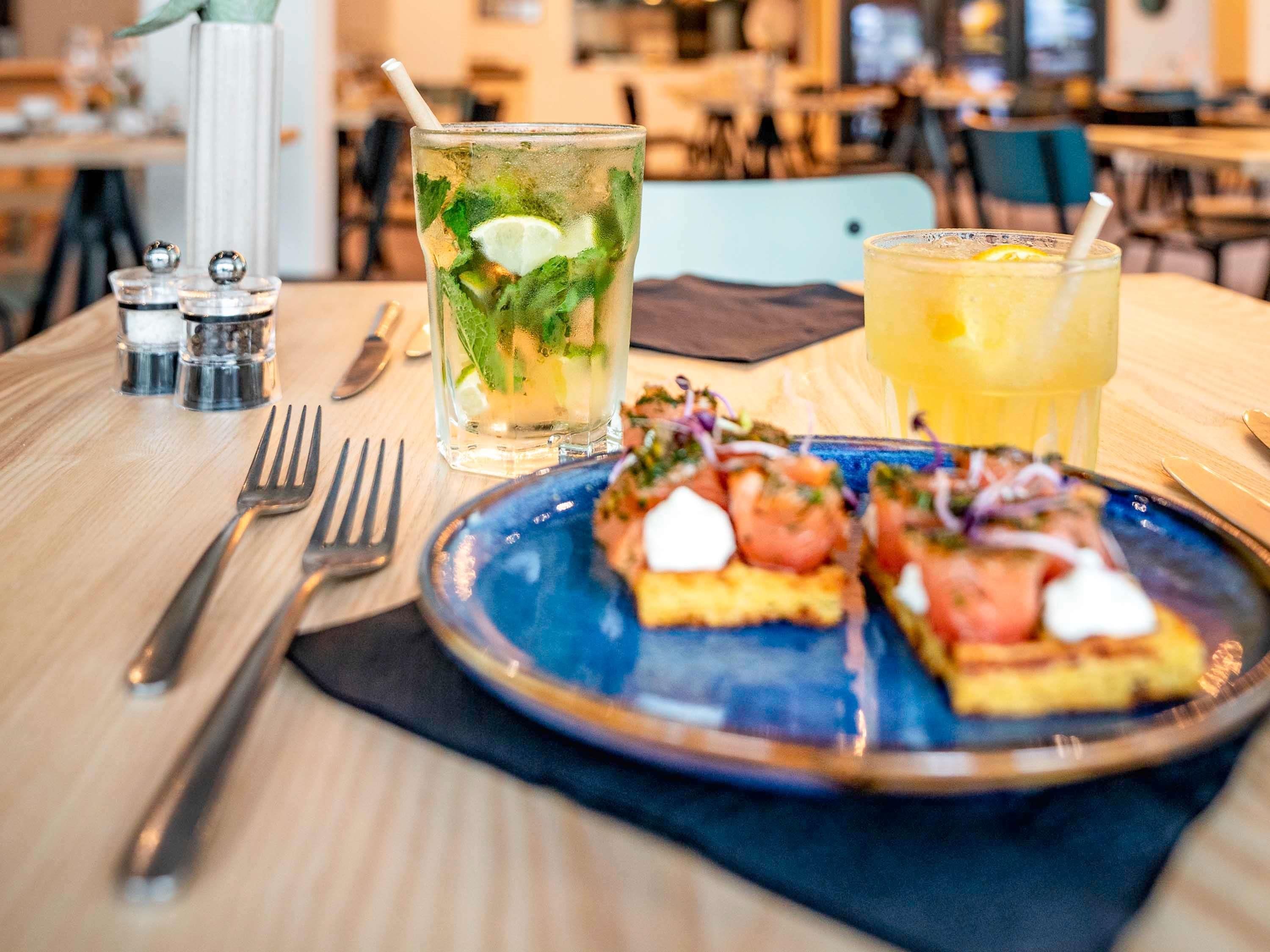 A dining table with a plate of food, two drinks, and salt and pepper shakers.