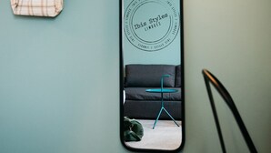 A mirror reflecting a room with a teal wall, a hanging plaid bag, and a black chair. - ibis Styles Limoges Centre (Limoges)