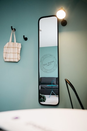 A mirror reflecting a room with a teal wall, a hanging plaid bag, and a black chair. - ibis Styles Limoges Centre (Limoges)