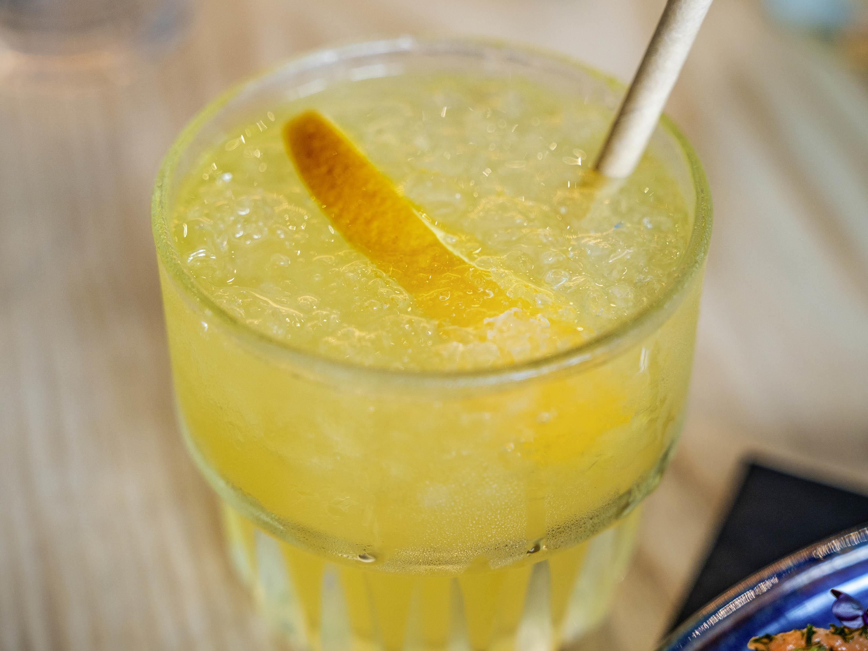 Ein Glas mit einem gelben Getränk, Eiswürfeln und einer Zitronenscheibe.