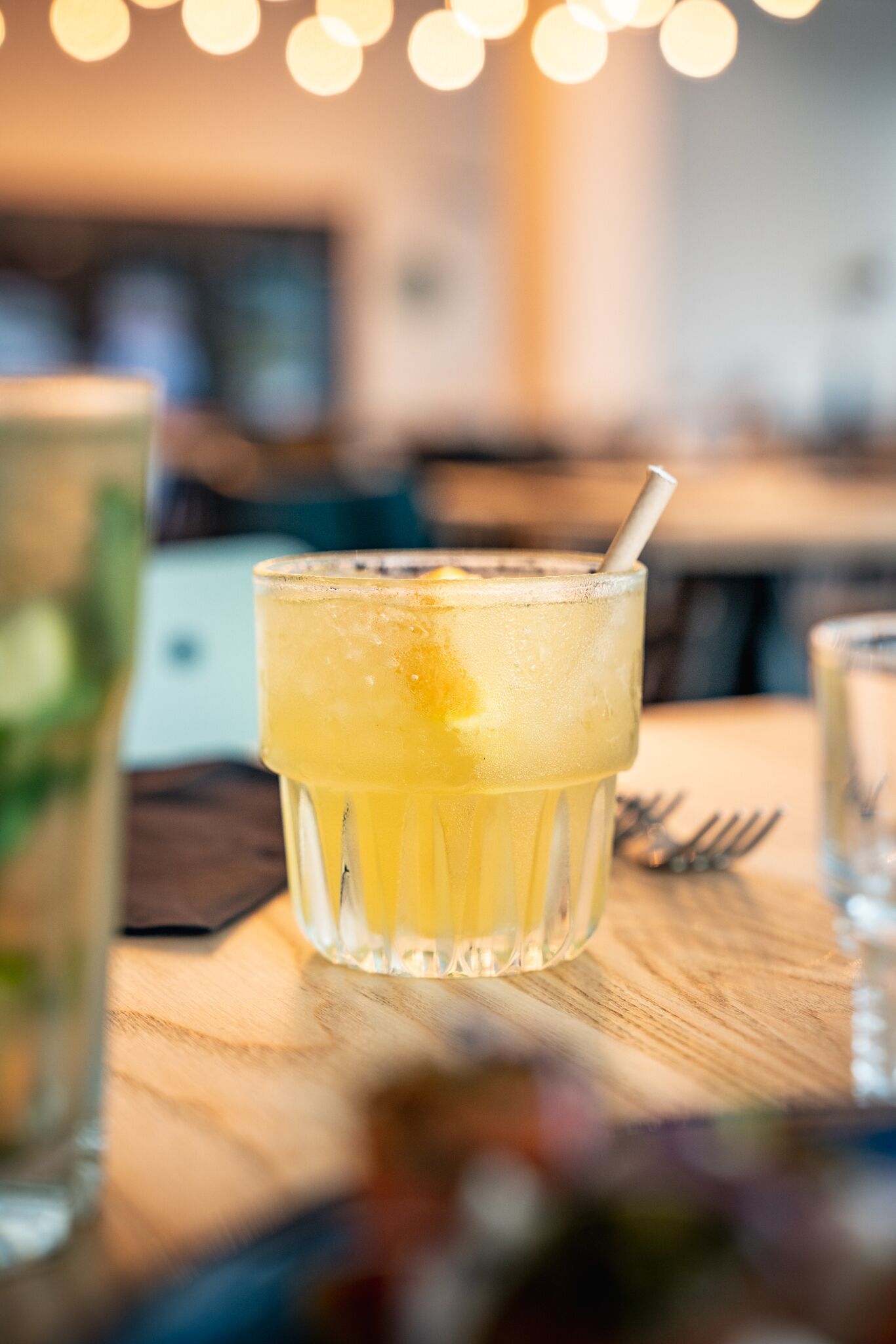 Un vaso de bebida amarilla con una pajita sobre una mesa de madera en un restaurante.