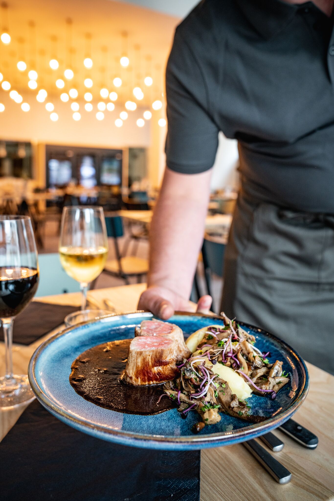A plate of food with a steak, mushrooms, and a dark sauce on a blue plate.