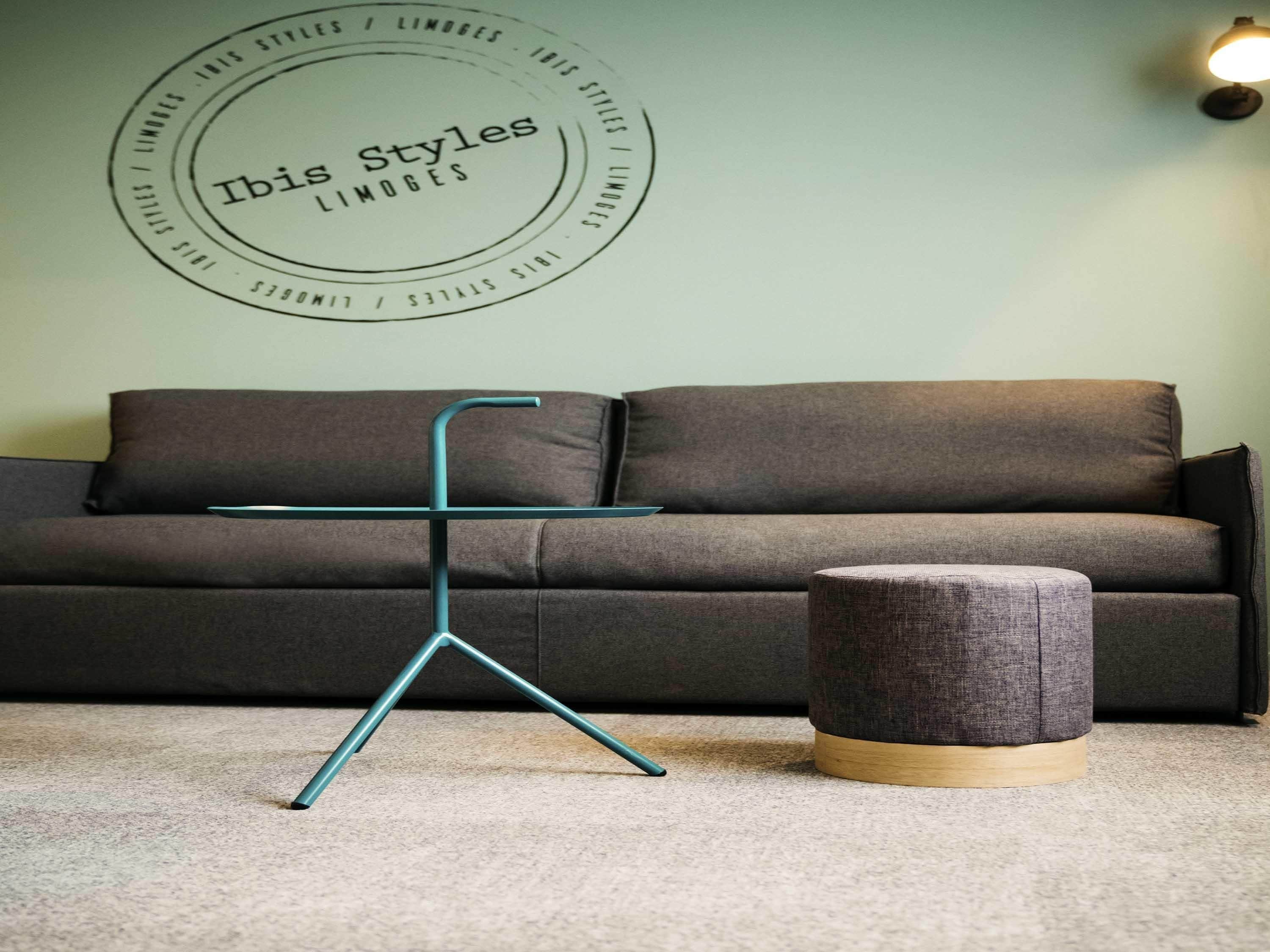 A room with a grey sofa, a teal metal stand, and a grey ottoman with a wooden base.
