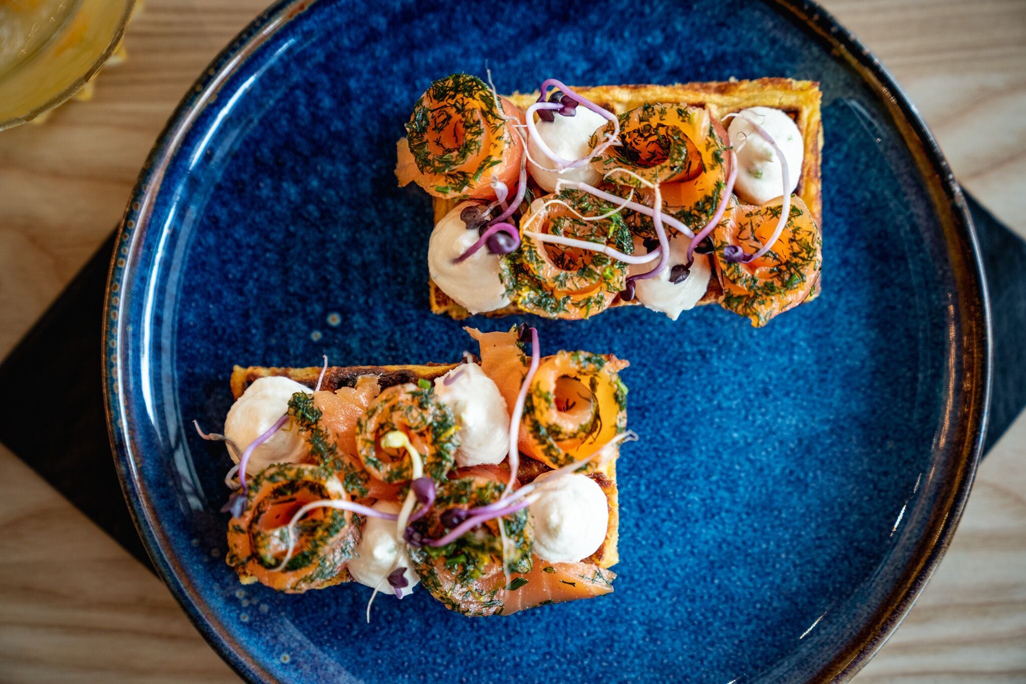 A blue plate with two pieces of food, each topped with salmon, cream, and greens.