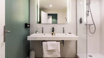 Un baño moderno con un espejo grande, dos lavamanos, una ducha y un cubo de basura.