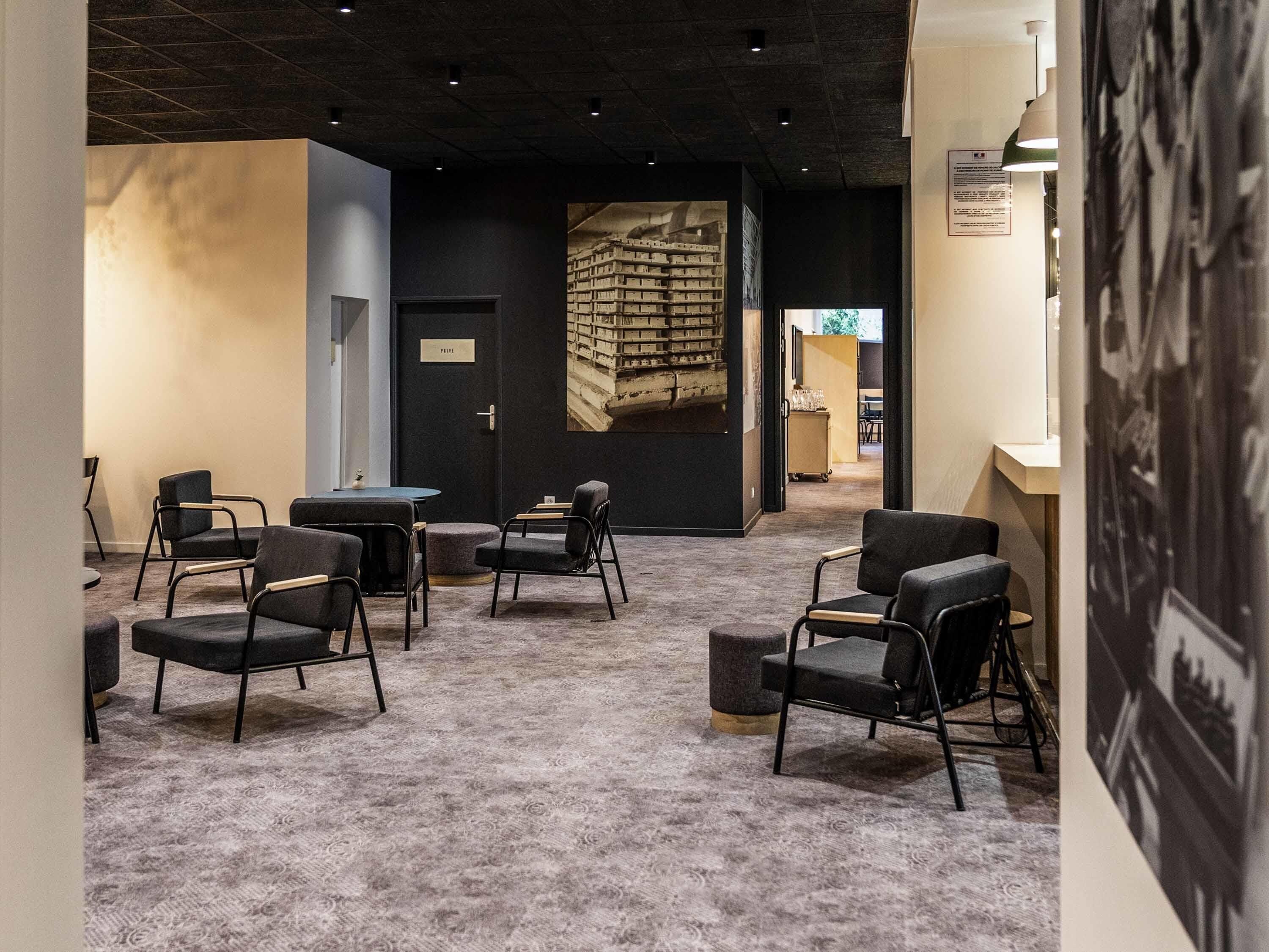 Un interior moderno con suelo alfombrado, sillas negras, una mesa redonda y una estantería.