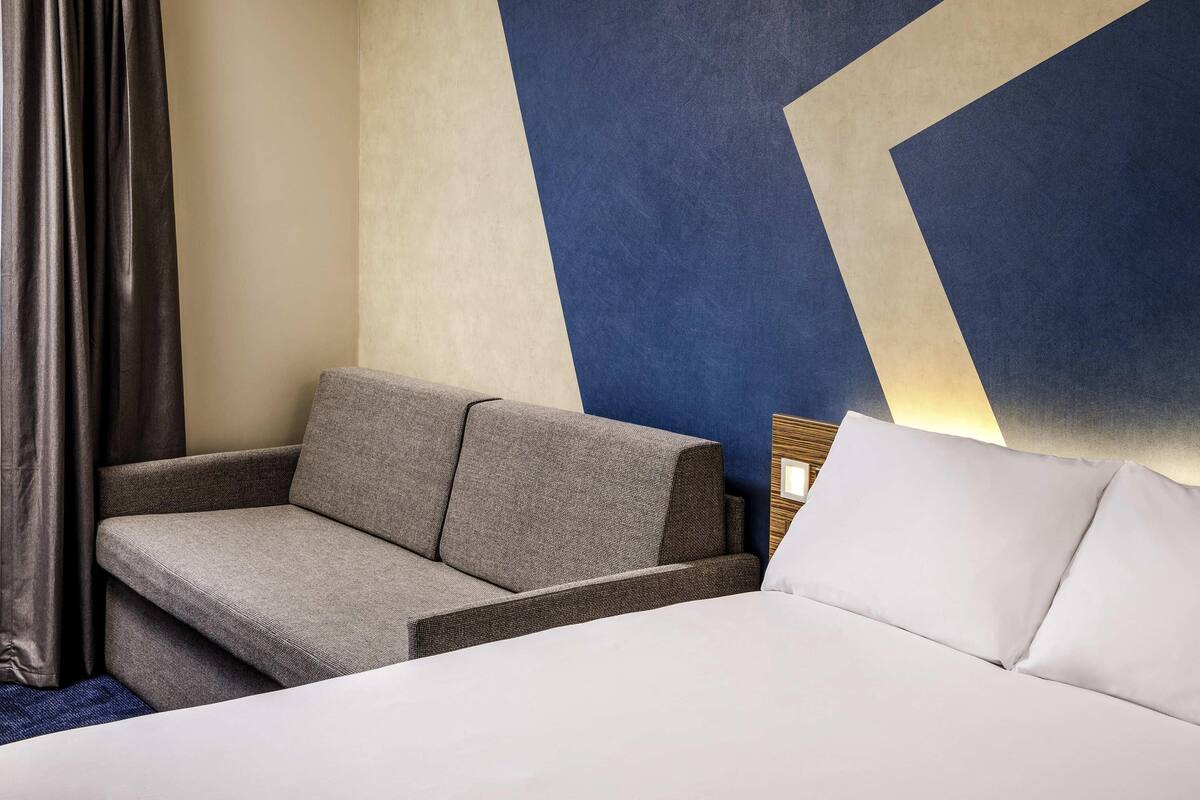 Ein Hotelzimmer mit Bett, Sofa, Wand mit geometrischem Muster und Vorhang.