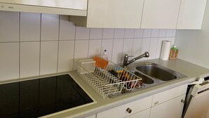 Una cocina con armarios blancos, un lavamanos de acero inoxidable y un escurreplatos.