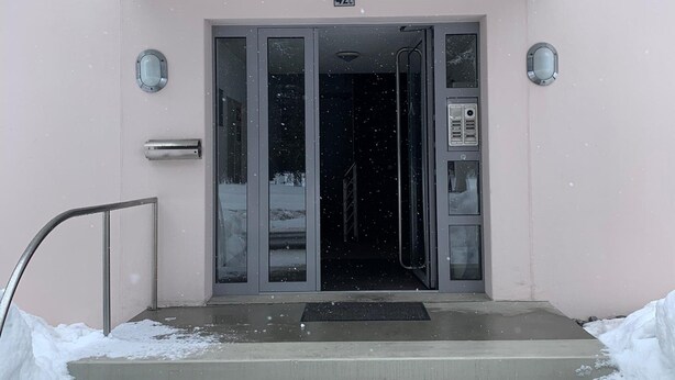 Entrada de un edificio con tejado nevado y puerta de cristal.