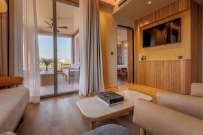 A modern living room with a sofa, armchair, and a coffee table. There is a sliding glass door leading to a balcony with a view. - Only YOU Hotel Malaga (Málaga)