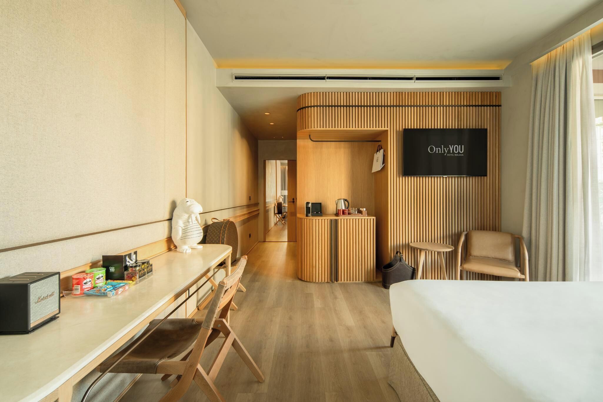 Habitación de hotel con cama, escritorio, silla, televisión y zona de recepción.