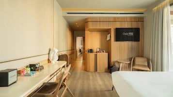 Habitación de hotel con cama, escritorio, silla, televisión y zona de recepción.