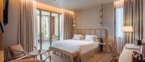 A hotel room with a bed, a desk, a chair, a small table, and a view of the outside.