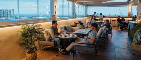 Un bar en la azotea con vista a la ciudad, muebles para sentarse y una planta en maceta.