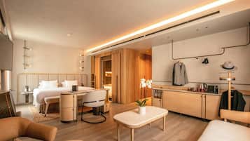 Habitación de hotel moderna con cama, escritorio, zona de estar y kitchenette.