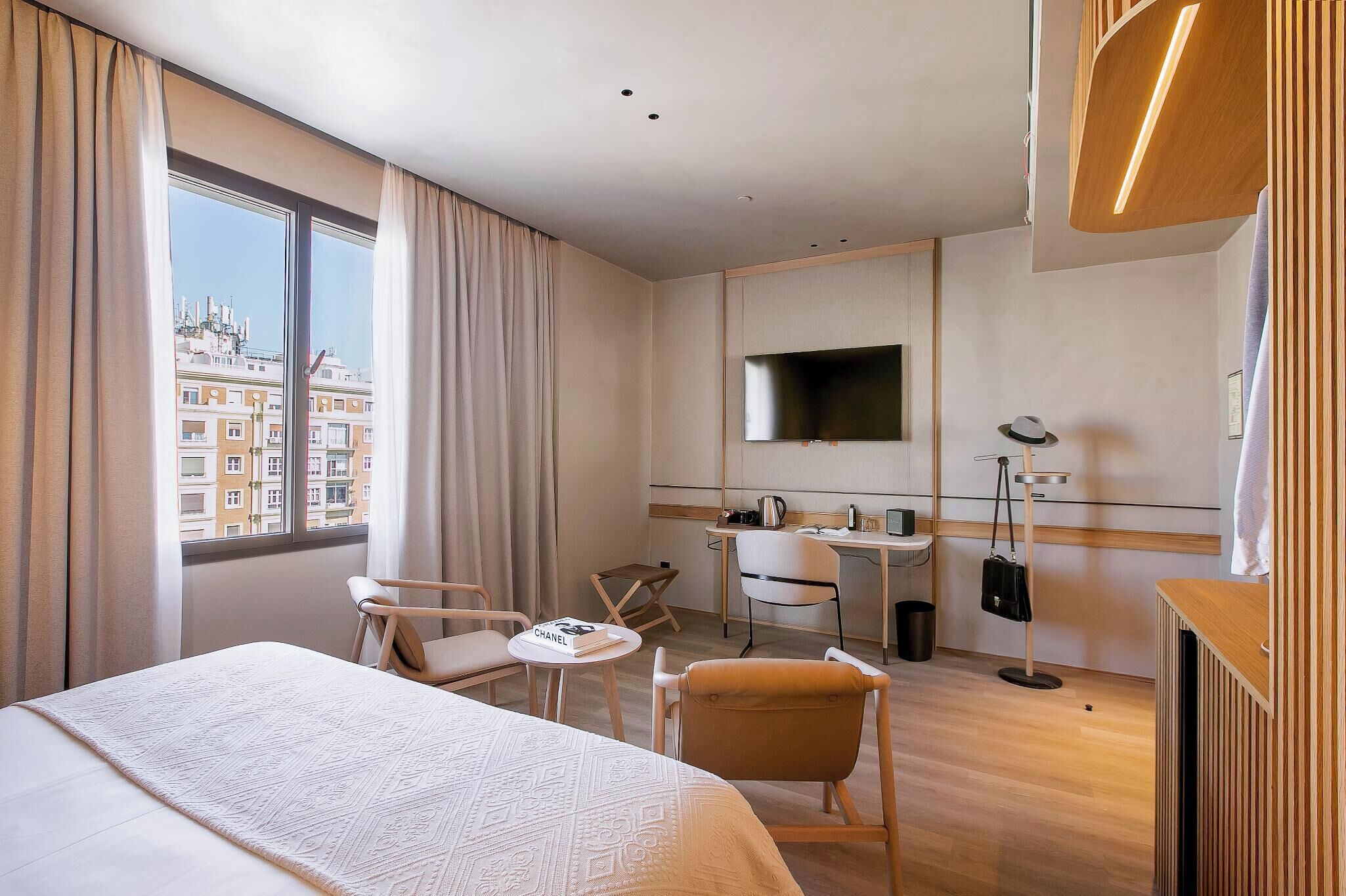 A hotel room with a bed, a desk, a chair, a TV, and a view of the city.