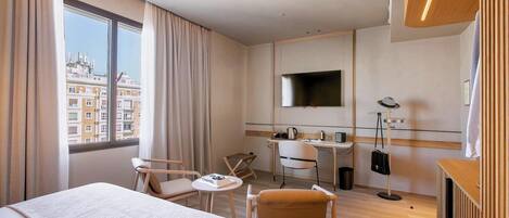 A hotel room with a bed, a desk, a chair, a TV, and a view of the city.