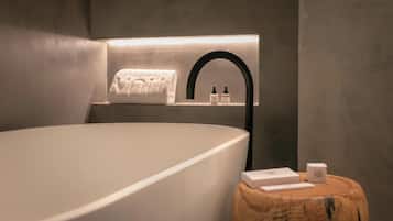 Un baño moderno con una bañera grande, una toalla colgada en un perchero de pared y artículos de aseo sobre una mesita de madera.
