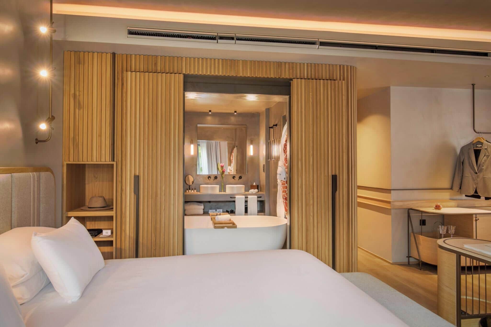 Habitación de hotel con una cama grande, un baño con bañera, un tocador con espejo y un escritorio con silla.