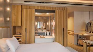 Habitación de hotel con una cama grande, un baño con bañera, un tocador con espejo y un escritorio con silla.