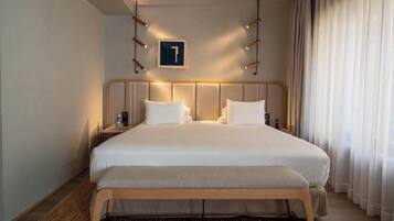 Habitación de hotel con una cama grande, una mesita de noche con una botella y vasos, un banco de madera, y un cartel con el número 1 en la pared.