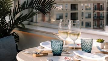 Una mesa redonda con dos copas de vino blanco, un vaso de vidrio estampado azul y una pequeña planta en maceta.