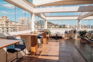 A modern rooftop terrace with a dining area, seating, and a view of the cityscape. - Only YOU Hotel Malaga (Málaga)
