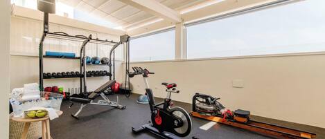 Un gimnasio con equipo de ejercicio, una máquina de remo y un estante en la pared con mancuernas.