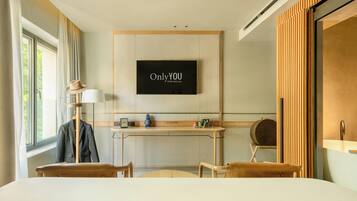 A hotel room with a bed, a desk, a chair, a television mounted on the wall, and a window with curtains.