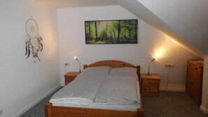 A bedroom with a wooden bed, a dreamcatcher, a forest painting, and bedside lamps. - Cozy vacation home 100 sqm in the middle of nature (Aerzen)