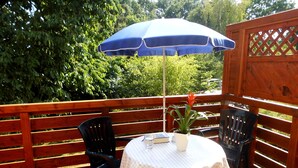 A wooden deck with a round table and chairs, a blue umbrella, and a potted plant. - Cozy vacation home 100 sqm in the middle of nature (Aerzen)
