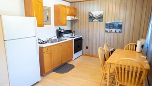 Una cocina compacta con armarios de madera, un refrigerador blanco, una estufa y un lavamanos. Hay dos sillas de madera alrededor de una mesa pequeña.