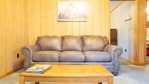 Un sofá de cuero marrón frente a paneles de madera, una mesa de centro de madera con una revista, y un cuadro en la pared.