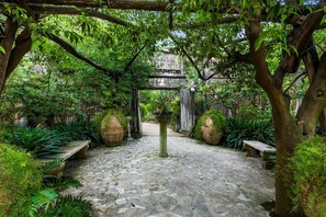 A stone-paved courtyard with large planters, a pergola, and lush greenery. - Deluxe Triple Library Room (SORRENTO)