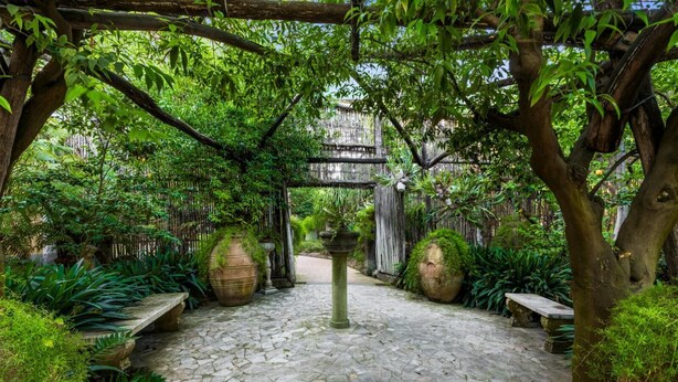 A stone-paved courtyard with a pergola, large planters, and lush greenery.